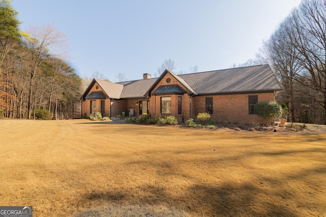 view of front of home featuring brick siding, a chimney, and a front yard