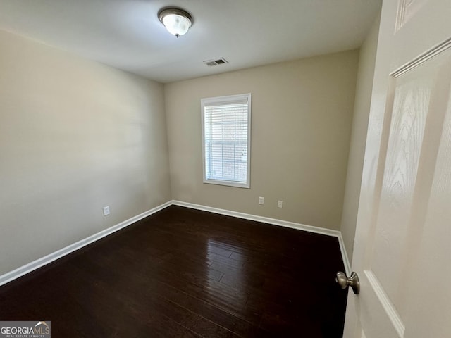 spare room featuring dark wood finished floors, visible vents, and baseboards