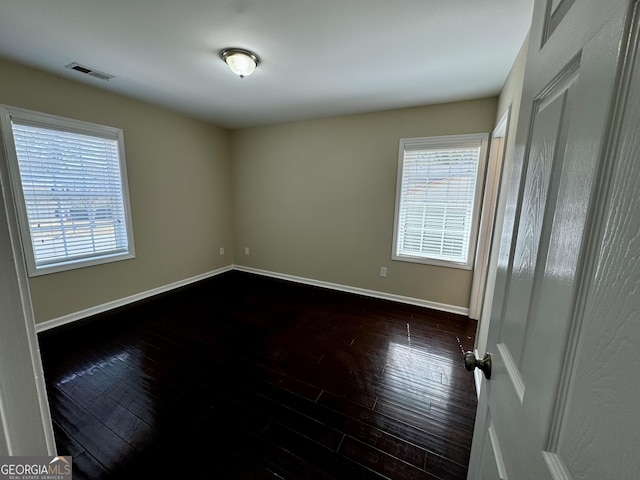 unfurnished room featuring visible vents, a healthy amount of sunlight, and dark wood-style flooring