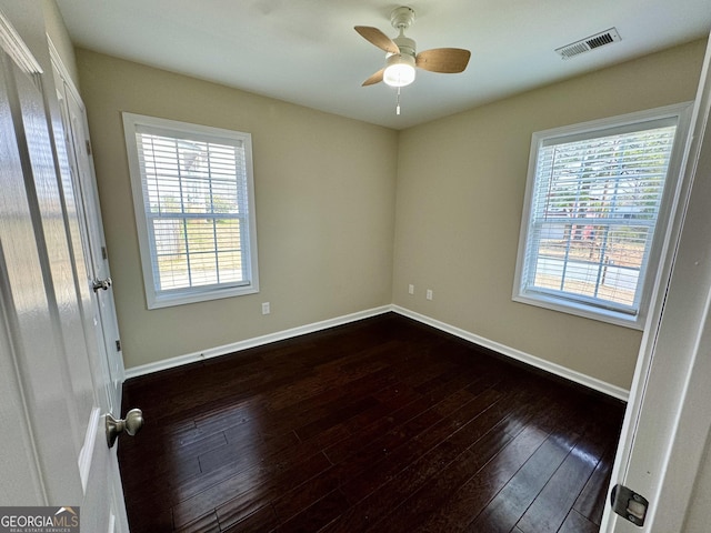 spare room with dark wood finished floors, visible vents, a healthy amount of sunlight, and baseboards