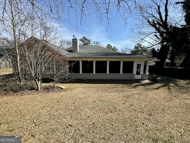 rear view of property with a yard, brick siding, a sunroom, and a chimney