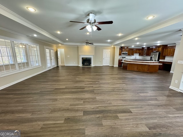 unfurnished living room with a tray ceiling, dark wood-style floors, a fireplace, crown molding, and baseboards