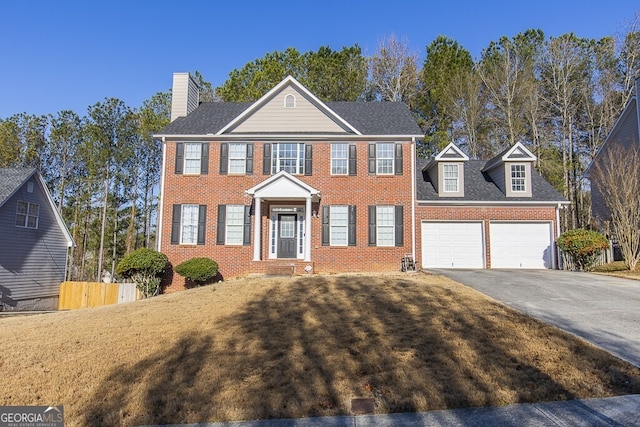 colonial inspired home featuring brick siding, fence, a chimney, a garage, and driveway