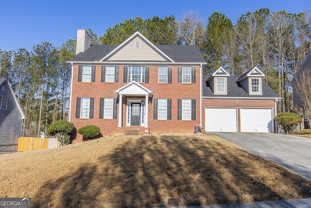 colonial house with fence, driveway, an attached garage, a front lawn, and brick siding