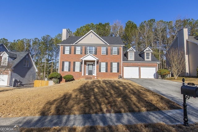 colonial inspired home with a garage, brick siding, driveway, and fence