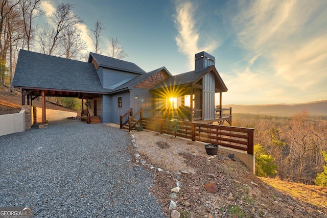 property exterior at dusk with board and batten siding, gravel driveway, and roof with shingles