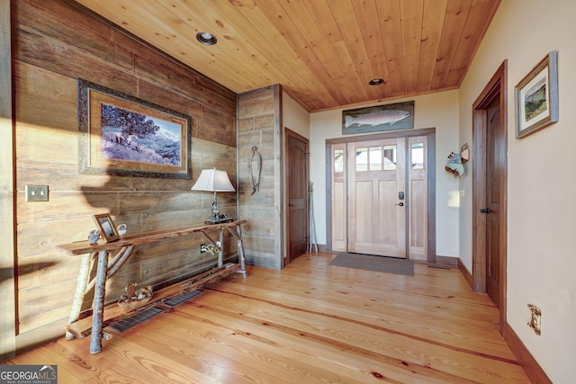 entryway with light wood-type flooring, visible vents, wooden ceiling, wood walls, and baseboards