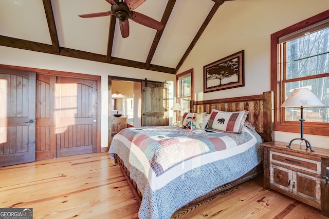 bedroom featuring beam ceiling, a barn door, and wood finished floors