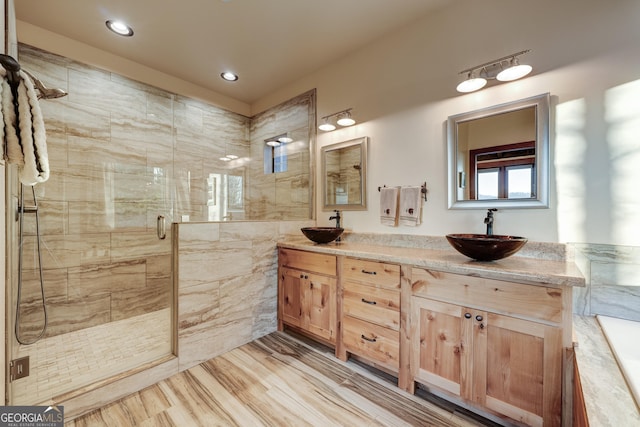 bathroom featuring a sink, wood finished floors, a stall shower, and double vanity