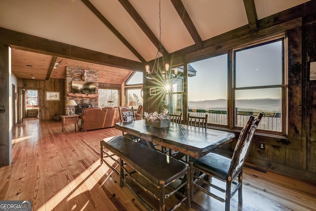 dining area with beam ceiling, a healthy amount of sunlight, a fireplace, and hardwood / wood-style flooring