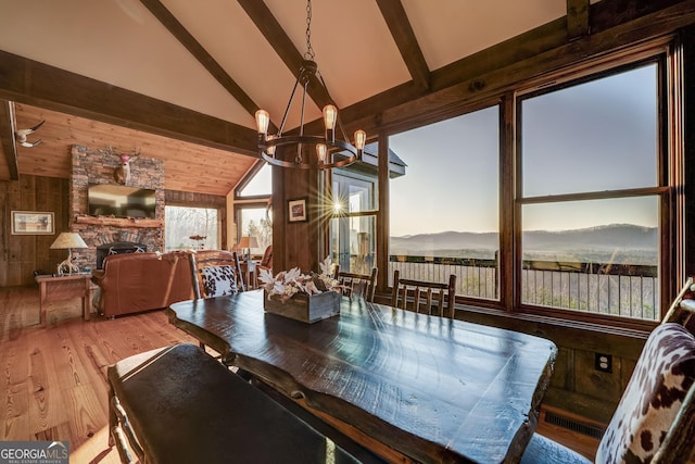 dining space with beamed ceiling, wood walls, a fireplace, and an inviting chandelier