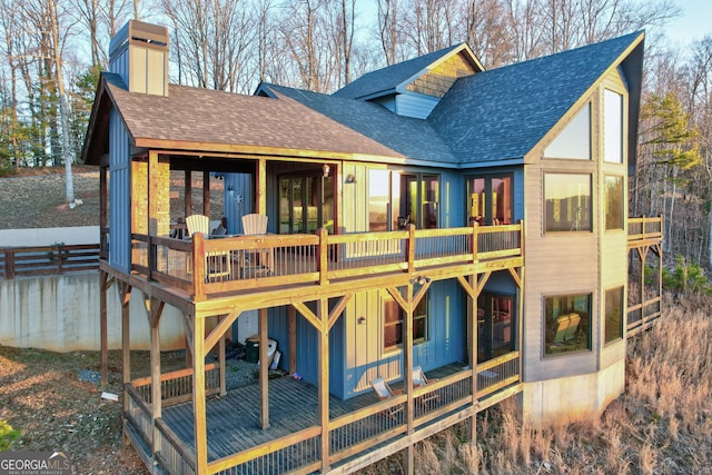 back of house with a wooden deck, board and batten siding, a chimney, and a shingled roof