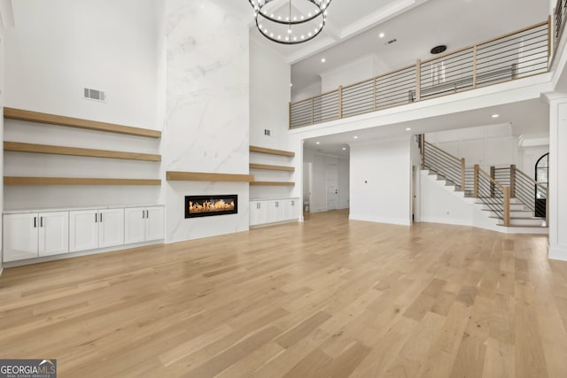 unfurnished living room with visible vents, a high ceiling, a high end fireplace, stairs, and light wood-type flooring