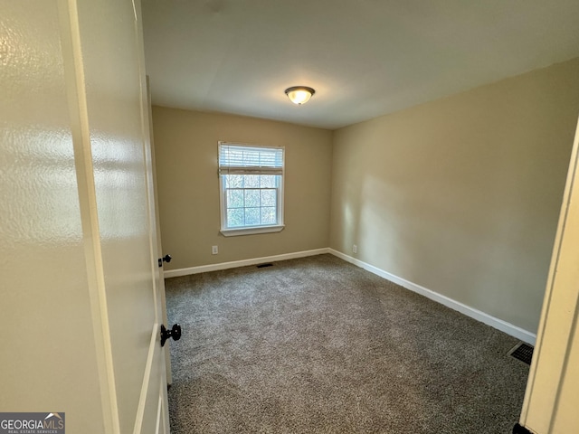 spare room featuring visible vents, baseboards, and dark carpet