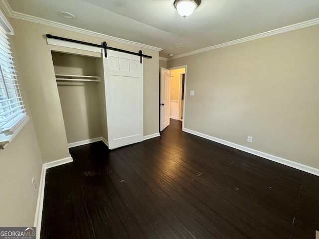 unfurnished bedroom with baseboards, dark wood finished floors, ornamental molding, a closet, and a barn door