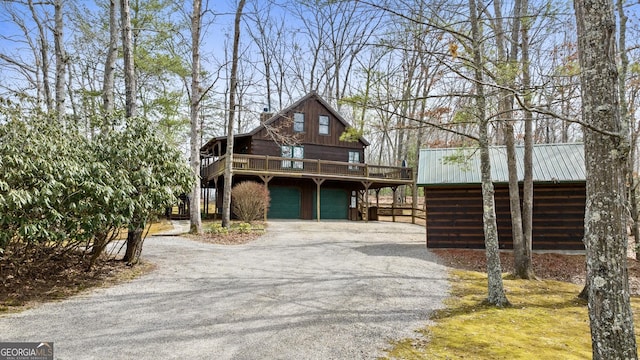 view of front of home featuring a garage, gravel driveway, a wooden deck, and metal roof