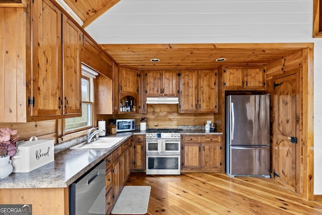 kitchen with under cabinet range hood, brown cabinets, appliances with stainless steel finishes, and a sink