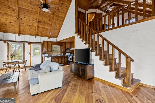 living room featuring stairway, beam ceiling, light wood-style flooring, wooden ceiling, and a ceiling fan