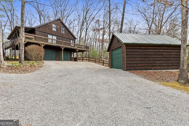 view of side of property featuring metal roof, a deck, a garage, an outdoor structure, and driveway