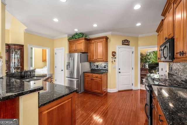 kitchen with brown cabinetry, dark wood-style floors, ornamental molding, a sink, and appliances with stainless steel finishes