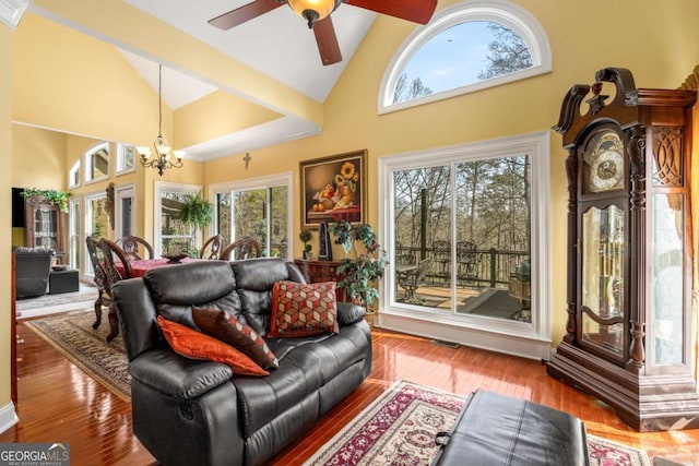 living area featuring a wealth of natural light, ceiling fan with notable chandelier, high vaulted ceiling, and wood finished floors