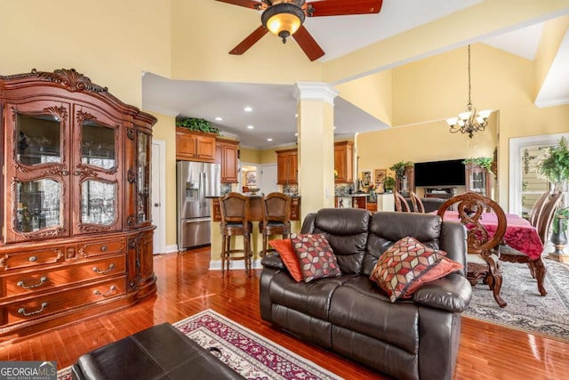 living area featuring wood finished floors, recessed lighting, ornamental molding, a towering ceiling, and ceiling fan with notable chandelier