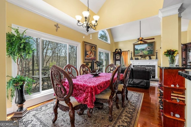 dining room featuring lofted ceiling, dark wood-style floors, a fireplace, and ceiling fan with notable chandelier