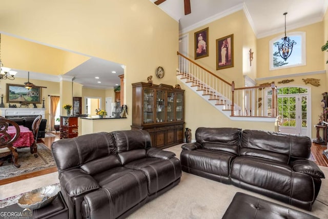 living area featuring stairway, a fireplace, ornamental molding, a towering ceiling, and ceiling fan with notable chandelier