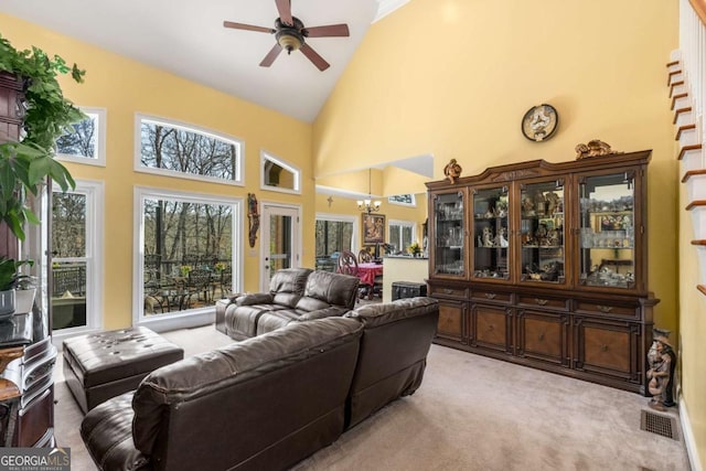 living area with visible vents, light colored carpet, high vaulted ceiling, and ceiling fan with notable chandelier
