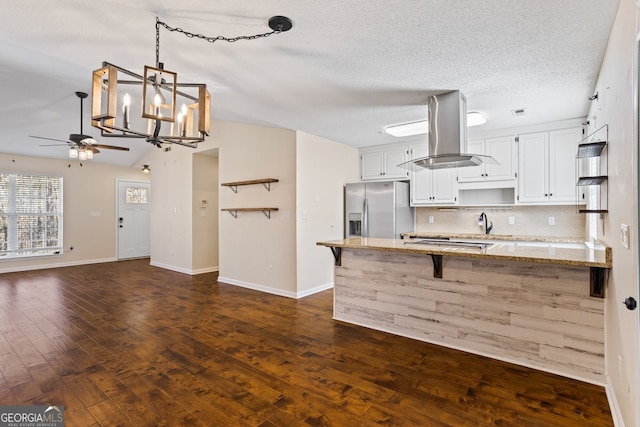 kitchen with backsplash, light stone countertops, stainless steel fridge with ice dispenser, a peninsula, and island range hood