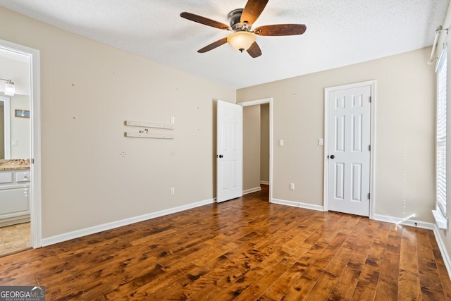 unfurnished bedroom with a textured ceiling, ensuite bath, hardwood / wood-style floors, baseboards, and ceiling fan