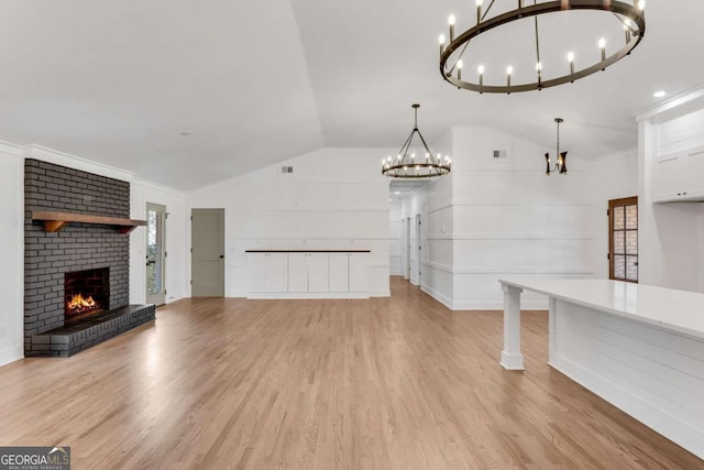 unfurnished living room with a chandelier, lofted ceiling, a brick fireplace, and light wood-style flooring