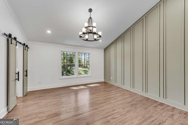 unfurnished room featuring ornamental molding, a barn door, light wood-style floors, a decorative wall, and a chandelier