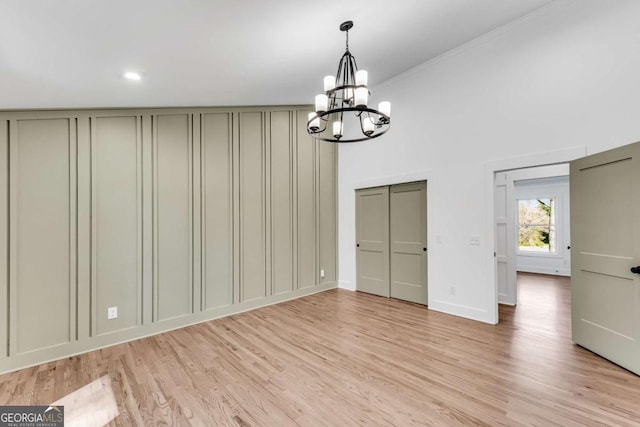 unfurnished dining area with a decorative wall, baseboards, an inviting chandelier, and light wood finished floors