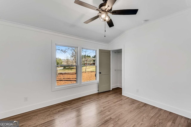 spare room featuring crown molding, baseboards, vaulted ceiling, wood finished floors, and a ceiling fan