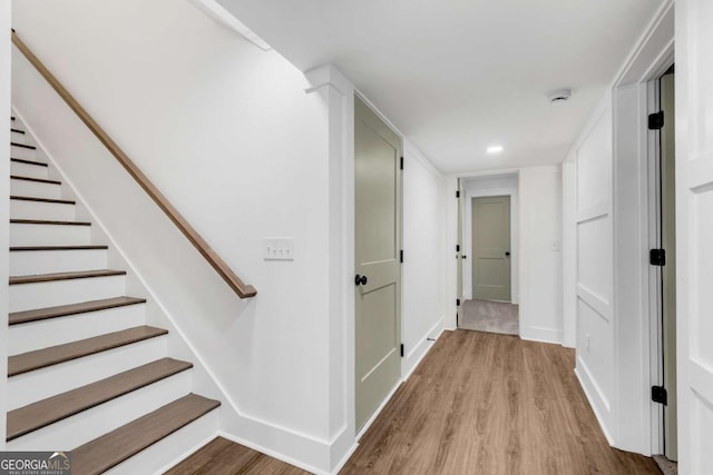 corridor featuring recessed lighting, baseboards, wood finished floors, and stairs