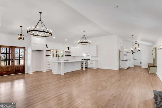 unfurnished living room with light wood finished floors, a sink, an inviting chandelier, and vaulted ceiling