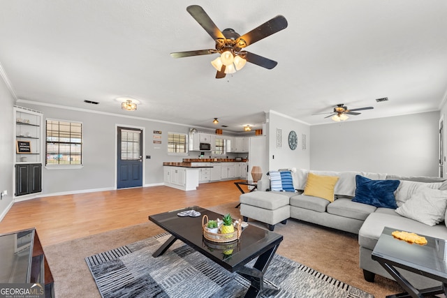 living room with visible vents, baseboards, crown molding, and light wood-style floors