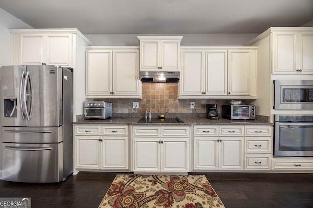 kitchen featuring under cabinet range hood, dark stone countertops, appliances with stainless steel finishes, and dark wood-style flooring