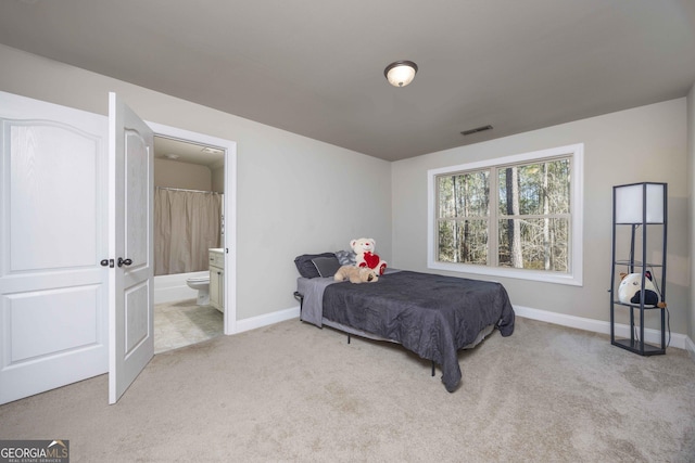 bedroom with visible vents, light colored carpet, ensuite bathroom, and baseboards