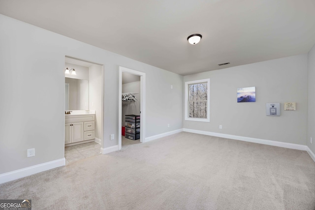 unfurnished bedroom featuring connected bathroom, a walk in closet, baseboards, light colored carpet, and a closet