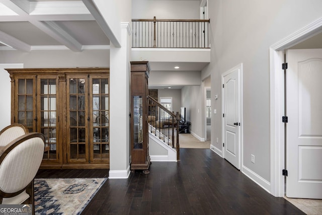 foyer entrance with stairway, baseboards, beam ceiling, hardwood / wood-style flooring, and a towering ceiling