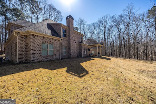 rear view of house featuring a yard, brick siding, and a chimney