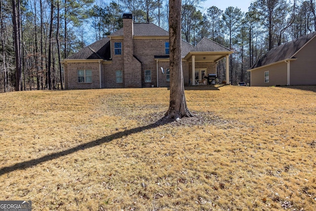 back of house featuring brick siding, a lawn, a chimney, and a shingled roof