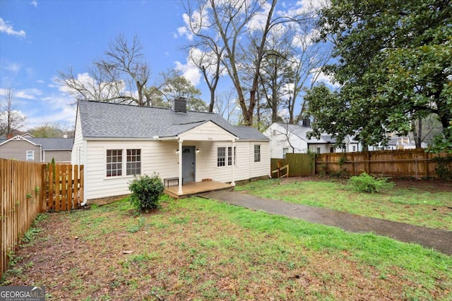 back of house with a yard, a chimney, a fenced backyard, and a shingled roof