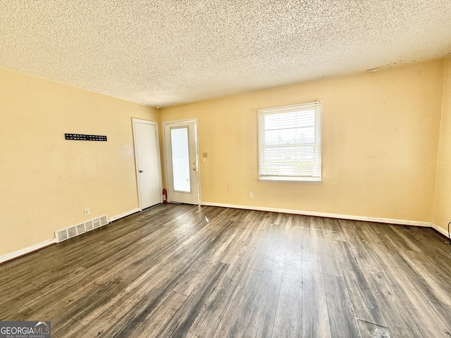 empty room with baseboards, visible vents, dark wood-style flooring, and a textured ceiling