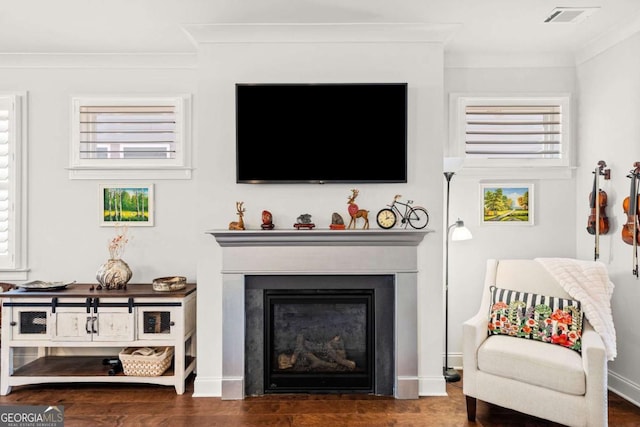 living area featuring a glass covered fireplace, visible vents, wood finished floors, and ornamental molding