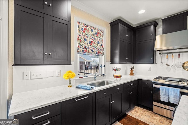 kitchen with wall chimney range hood, gas stove, dark cabinets, and a sink