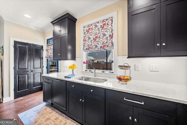 kitchen featuring a sink, backsplash, light stone countertops, light wood-style floors, and dark cabinets