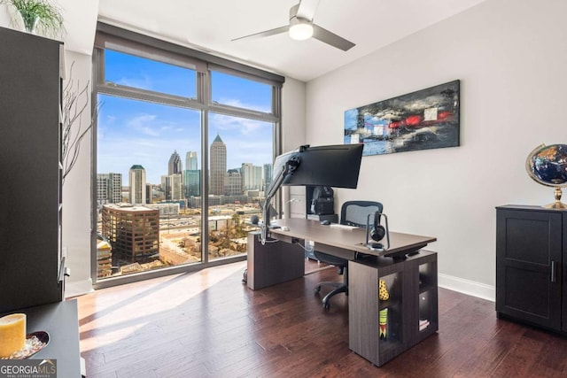 office area with ceiling fan, baseboards, a city view, a wall of windows, and wood finished floors